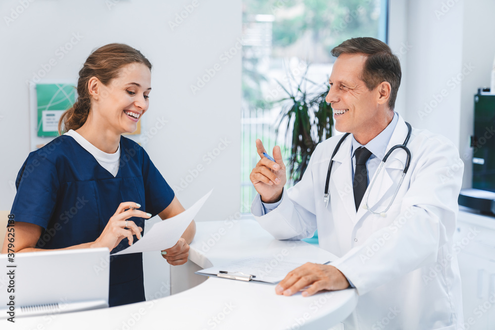 Senior doctor talking with nurse receptionist at hospital reception Senior doctor talking with nurse receptionist at hospital reception