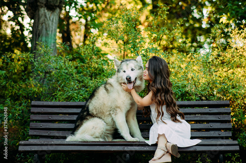 Young dwarf woman sits on bench next to Malamute dog and hugs it. photo