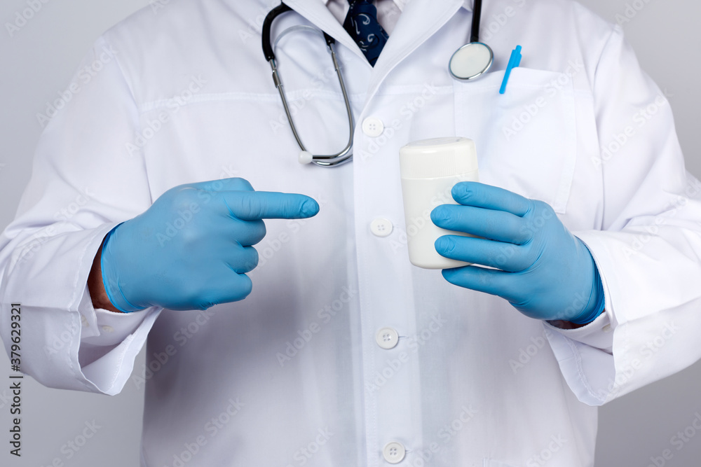 doctor in a white medical coat and blue latex gloves holds a white plastic jar of pills