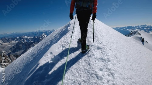 Last steps before Mont Blanc (Monte Bianco) summit 4,808 m of man with climbing axe dressed mountaineering clothes, boots with crampons walking in rope team. Handheld rear team member camera view.