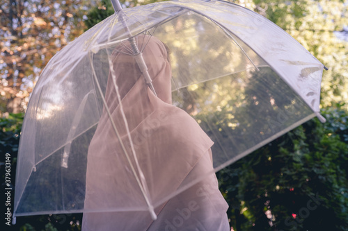 Autumn. Lonely muslim woman in a headscarf under a transparent umbrella with rain drops walking in a park, garden. Rainy day landscape. Vintage Toned