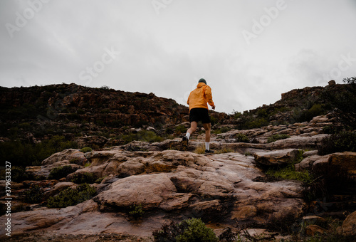 Athletic young male running up rocky side of mountain on wet stones in cloudy weather with rocky hills