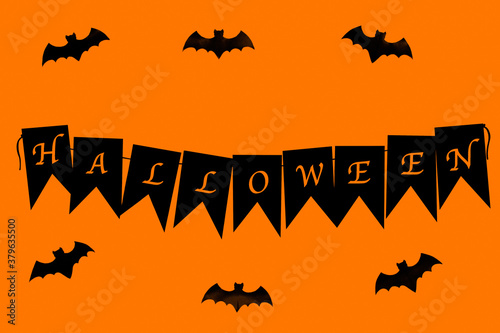 Halloween lettering on black flags. Nearby are figures of bats. On an orange background.