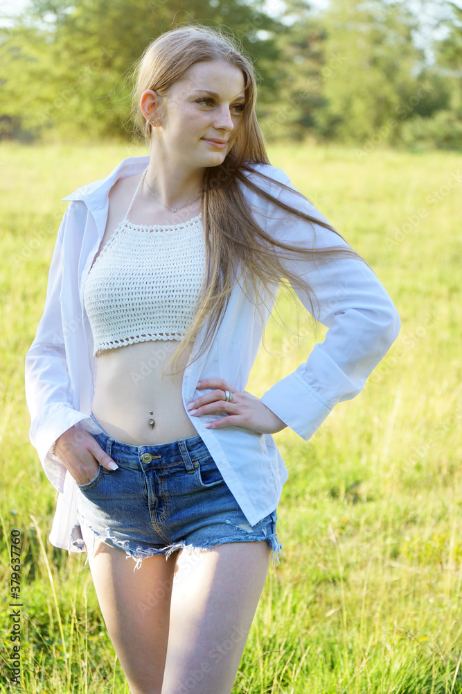 Hübsche junge Frau trägt Hot Pants, offene Bluse und Oberteil bauchfrei und  lächelt freundlich an einem sonnigen Sommertag im Park Stock Photo | Adobe  Stock