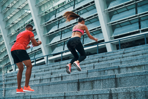 Fit young couple in sports clothing jumping while exercising on the steps outdoors