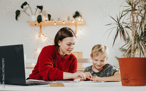 Tutoring. Home schooling. Teacher and pupil. A woman and a blonde boy at the table.