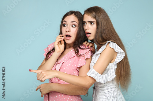 Young surprised girlfriends in fashion dresses on blue background