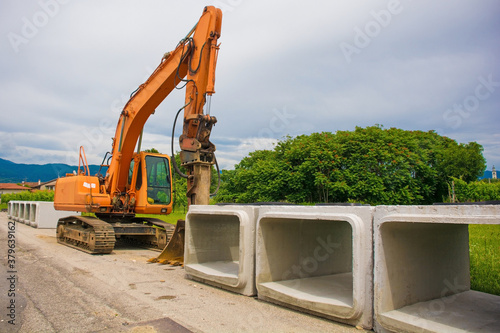 A crawler excavator with a rotating house platform and continuous caterpillar track with some reinforced concrete box culverts. On the site of a sewage system replacement scheme in north west Italy

