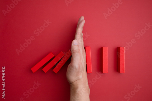 red domino blocks that begins to fall and a hand that prevents it from falling.