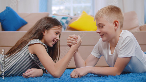 Фотография Happy boy and his sister arm wrestling laying on the floor in living room