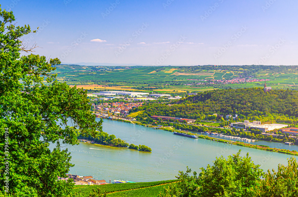 Aerial panoramic view of river Rhine Gorge or Upper Middle Rhine Valley with vineyards green fields, trees forest hill and small towns on bank, blue sky, Rhineland-Palatinate, Hesse states, Germany