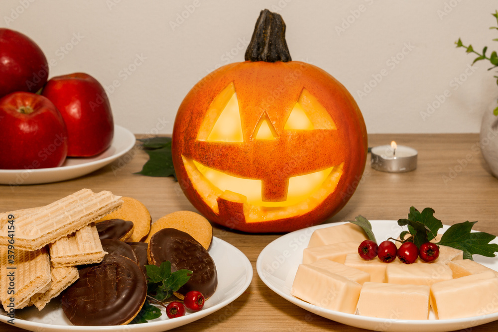 Next to the candles is a pumpkin with a carved face. Sweets for Halloween on the table. Next to the candles is a pumpkin with a carved face. Sweets for Halloween on the table.
