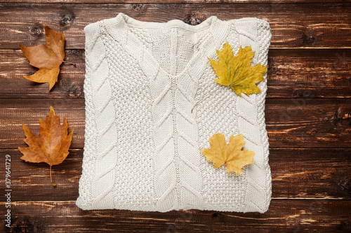 Woolen sweater with autumn leafs on brown wooden table