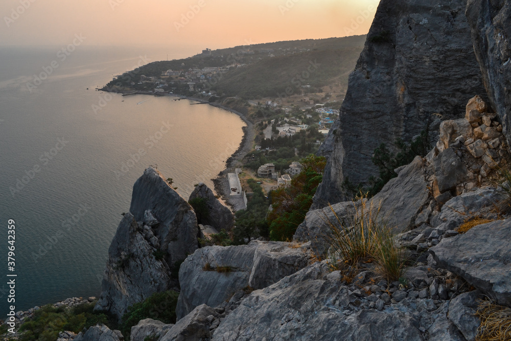 sunset stones rock cliff, shore, coast of bay of Black sea, town among hills and high mountains. Crimea, Russia, summer landscape