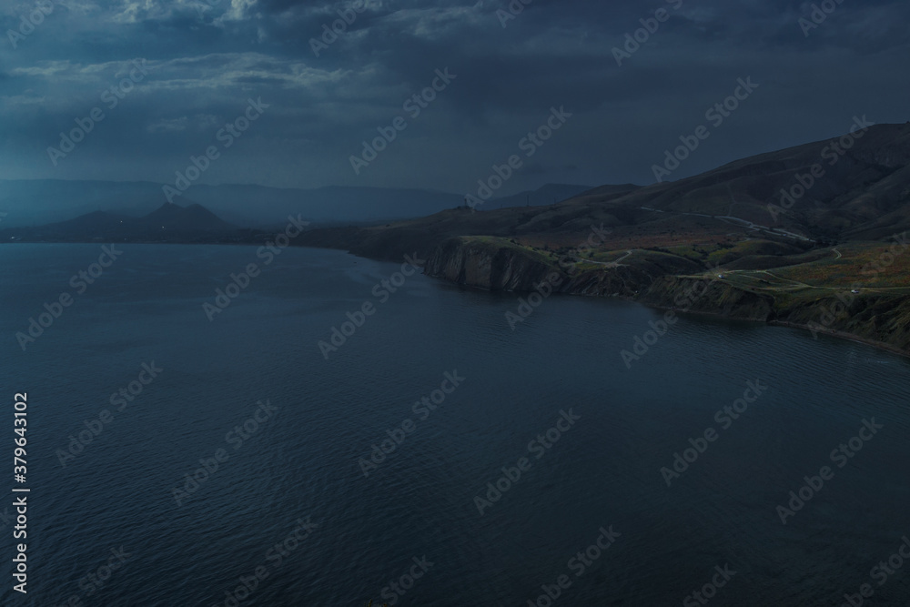 view of beautiful dark coast with road of bay of sea with water among hills and high mountains. Crimea, Russia, evening cloudy landscape
