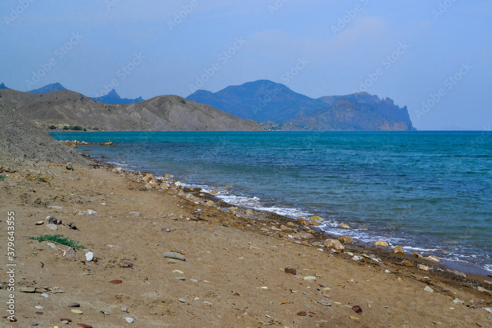 view of beautiful sand pebbles coast of bay of sea with blue emerald water among hills and high mountains. Crimea, Russia, summer landscape