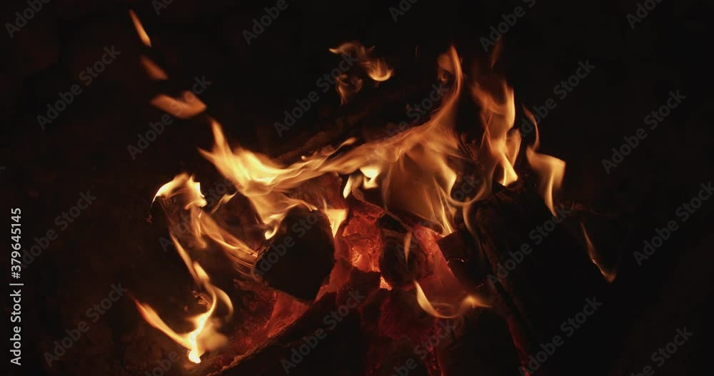 Close up campfire burning with orange light outdoors on black night background. Logs glowing in fire flame slow motion copy text space. Camping travel adventure. Danger safety inflammation Close up campfire burning with orange light outdoors on black night background. Logs glowing in fire flame slow motion copy text space. Camping travel adventure. Danger safety inflammation