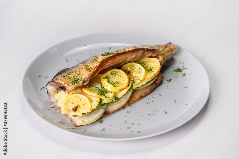 Close up of baked mackerel with lemon slices and onion on gray plate isolated on gray background. Grilled fish served with fresh herb dill. Food isolation 
