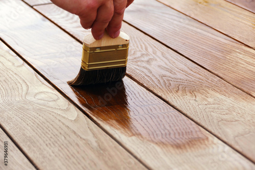 Male hand paints with a broad brush wood oil on thermo-ash, painting wooden boards