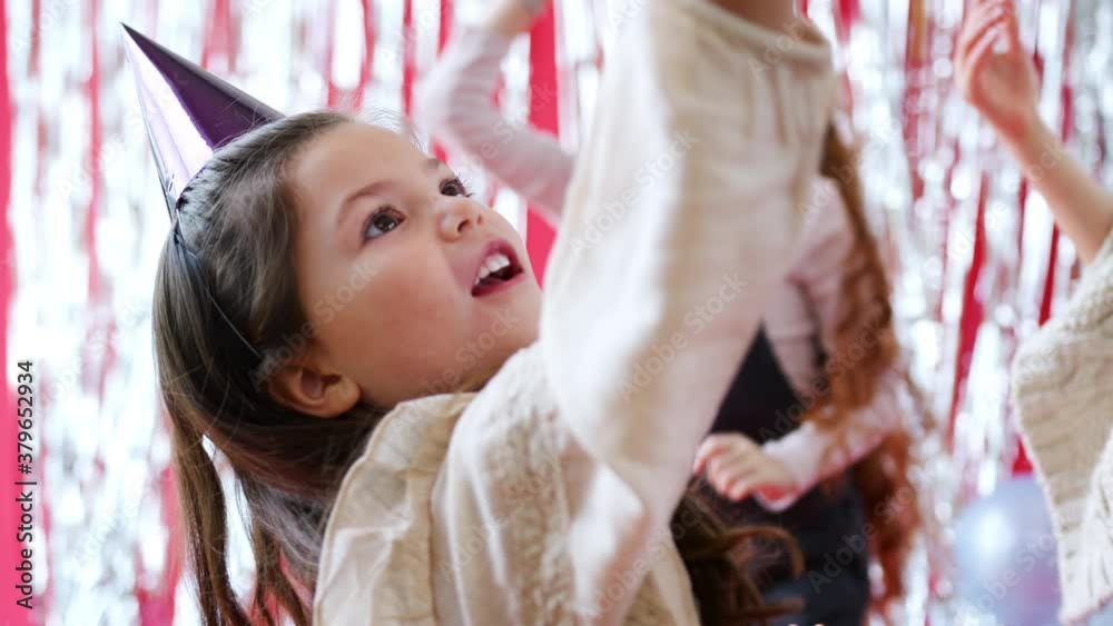 Group of children celebrating at birthday party with paper hats playing with balloons - shot in slow motion Group of children celebrating at birthday party with paper hats playing with balloons - shot in slow motion