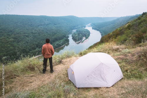 A tourist stands near a tent on the top of a mountain above the majestic Dniester River in Ukraine. Landscape photography
