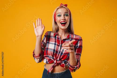 Image of cheerful pinup girl waving hand and pointing finger at camera