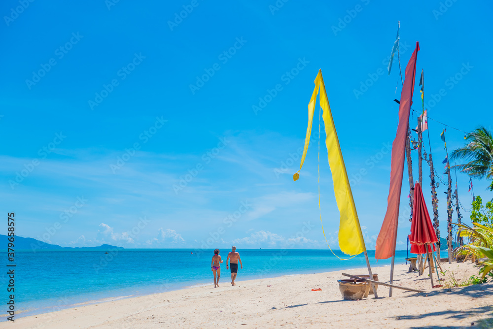 people walk along the beach on the paradise island of koh samui in thailand, white beach and turquoise sea, palm trees and flags on the seashore, vacation in the tropics people walk along the beach on the paradise island of koh samui in thailand, white beach and turquoise sea, palm trees and flags on the seashore, vacation in the tropics