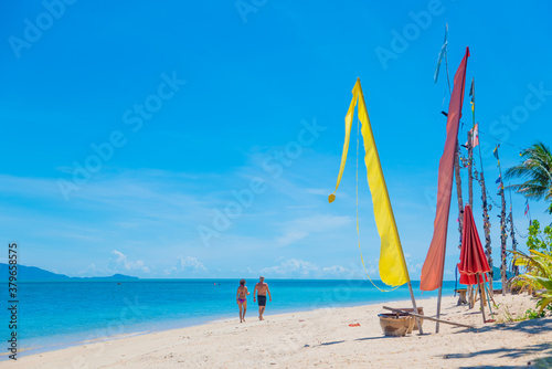 people walk along the beach on the paradise island of koh samui in thailand, white beach and turquoise sea, palm trees and flags on the seashore, vacation in the tropics