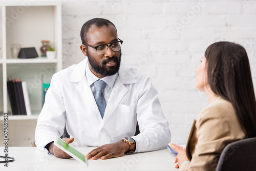 selective focus of african american doctor in eyeglasses holding digital tablet with green screen near patient photo