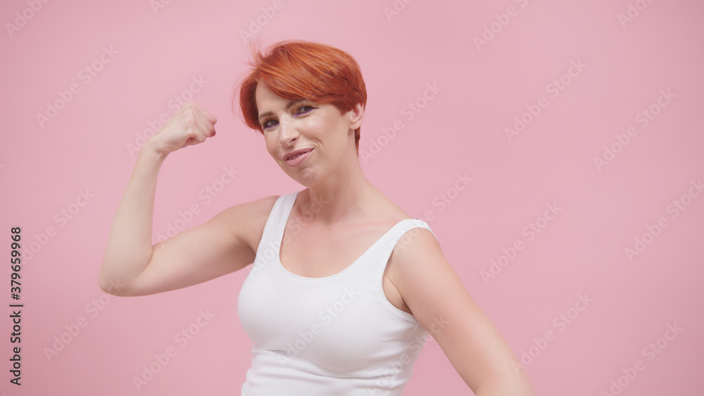 Beautiful excited middle aged redhead woman flexing her muscles, isolated on pink purple background. High quality photo Beautiful excited middle aged redhead woman flexing her muscles, isolated on pink purple background. High quality photo