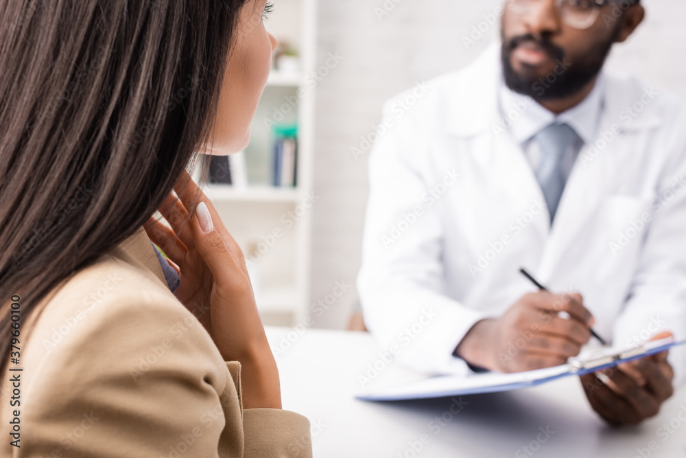 Fototapeta premium selective focus of diseased woman touching sore throat near african american doctor holding clipboard