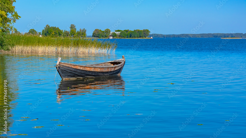 Landscape on the Kizhi island in Lake Onega on a summer sunny day. Lonely wooden fishing boat on the lake, among the aquatic vegetation. In the distance, the opposite shore of the lake Landscape on the Kizhi island in Lake Onega on a summer sunny day. Lonely wooden fishing boat on the lake, among the aquatic vegetation. In the distance, the opposite shore of the lake