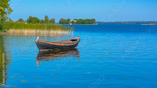 Landscape on the Kizhi island in Lake Onega on a summer sunny day. Lonely wooden fishing boat on the lake, among the aquatic vegetation. In the distance, the opposite shore of the lake