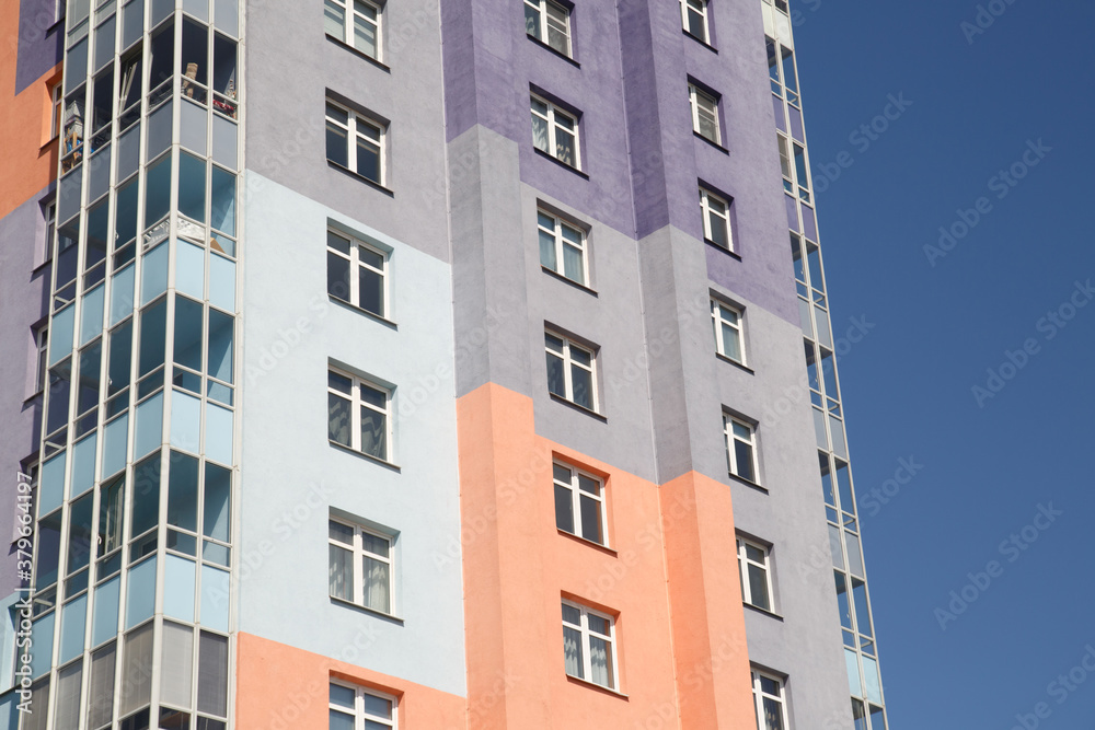 Part of a wall with windows of a multi-colored apartment building against the background of the sky.