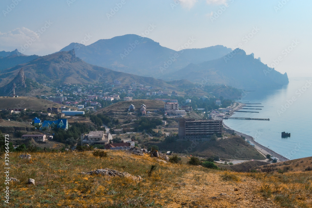 top view of resort town on shore of Black Sea bay among mountains and sharp rocks, blue water, summer, sunset steppe with bushes in the foreground