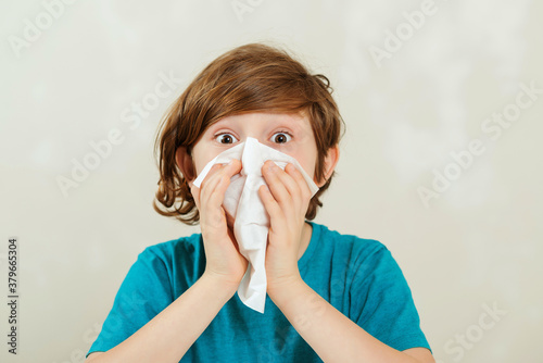 Boy blowing runny nose. Sick boy sitting at desk. Kid using paper napkins. Allergic kid, flu season.