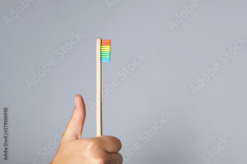 Hand hold rainbow bamboo eco tooth brush. colorful. Dental care. Morning oral routine. Grey background with shadow. Copy space. Washing prevention hygiene. Horizontal photo