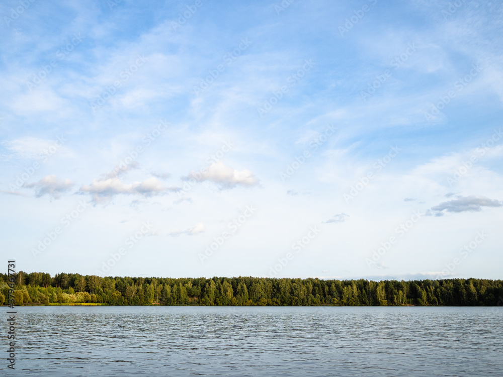 blue sky with spindrift clouds over lake and forest on horizon at September sunset