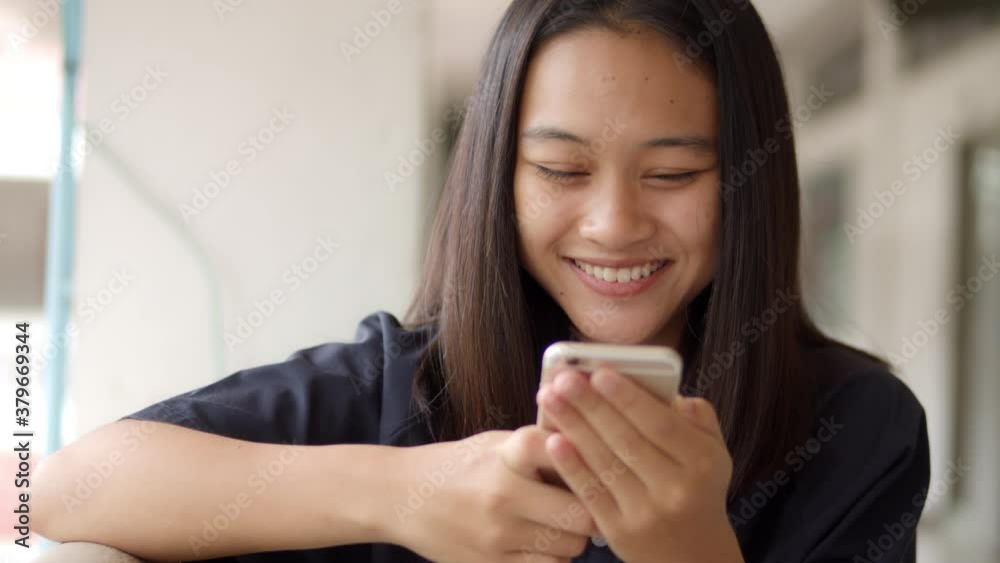 A smiling and laughing Asian teenage girl enjoy funny social media on her mobile phone.
