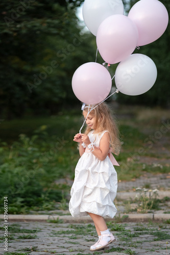 Little girl in white dress with balloons on the street
