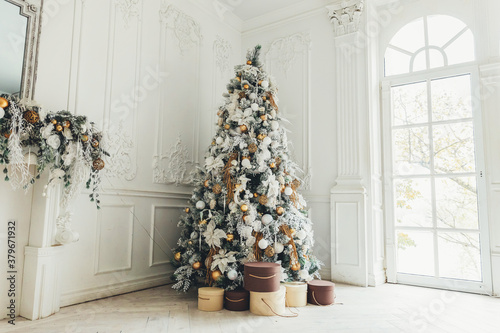 Classic christmas New Year decorated interior room New year tree. Christmas tree with gold decorations. Modern white classical style interior design apartment, large window. Christmas eve at home.