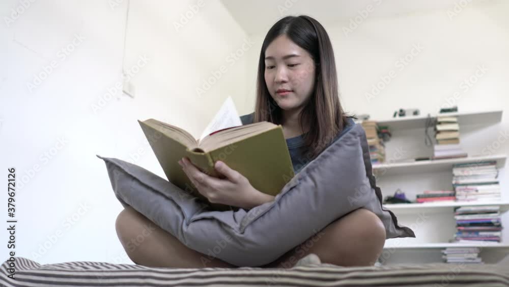 Asian beautiful woman reading book at home. Teenages girl sittinng on bed and happy with textbook while being quarantine at home. Stay at home education concept. Asian beautiful woman reading book at home. Teenages girl sittinng on bed and happy with textbook while being quarantine at home. Stay at home education concept.