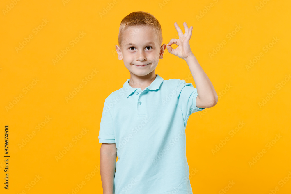 Smiling handsome little male fair-haired brown-eyed kid boy 5-6 years old wearing stylish blue turquoise t-shirt polo showing ok gesture isolated on yellow color wall background, child studio portrait Smiling handsome little male fair-haired brown-eyed kid boy 5-6 years old wearing stylish blue turquoise t-shirt polo showing ok gesture isolated on yellow color wall background, child studio portrait