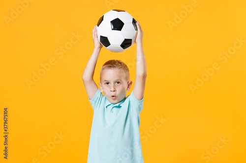 Fun inspired little kid boy 5-6 years old football fan in blue t-shirt cheer up support favorite team, hold in hands soccer ball isolated on yellow background. Sport family leisure lifestyle concept. © ViDi Studio