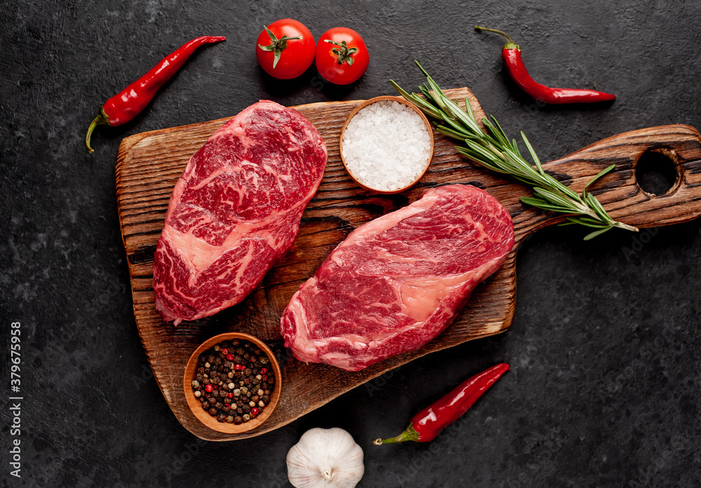 Two raw beef ribeye steaks with spices on a stone background - obrazy, fototapety, plakaty 