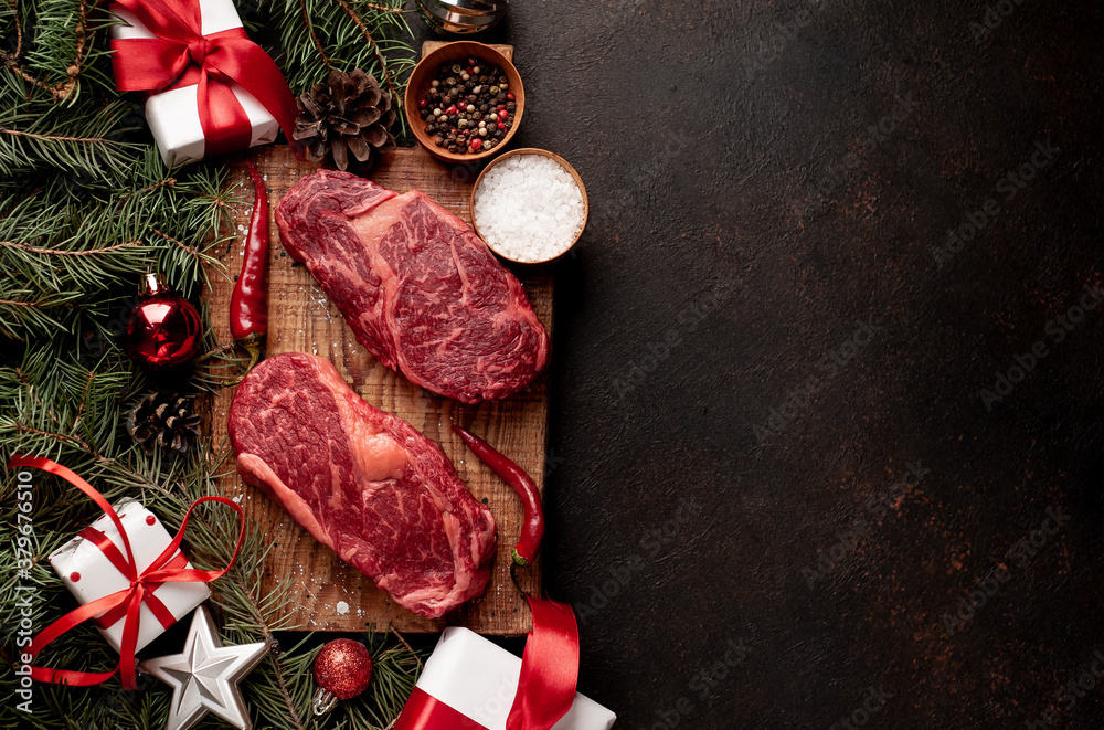 Raw ribeye beef steaks for preparing a dinner for two for a Christmas holiday on a stone table with a Christmas tree and Christmas tree decorations with copy space	