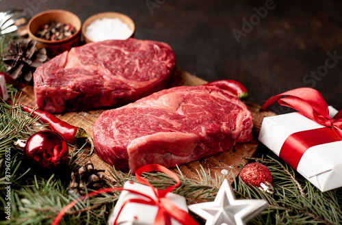 Raw ribeye beef steaks for preparing a dinner for two for a Christmas holiday on a stone table with a Christmas tree and Christmas tree decorations with copy space