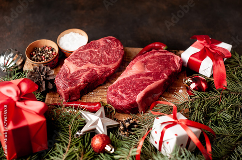 Raw ribeye beef steaks for preparing a dinner for two for a Christmas holiday on a stone table with a Christmas tree and Christmas tree decorations with copy space