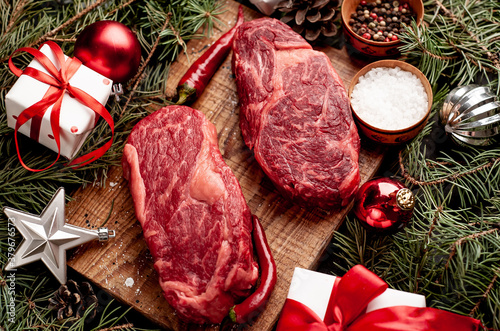 Raw ribeye beef steaks for preparing a dinner for two for a Christmas holiday on a stone table with a Christmas tree and Christmas tree decorations