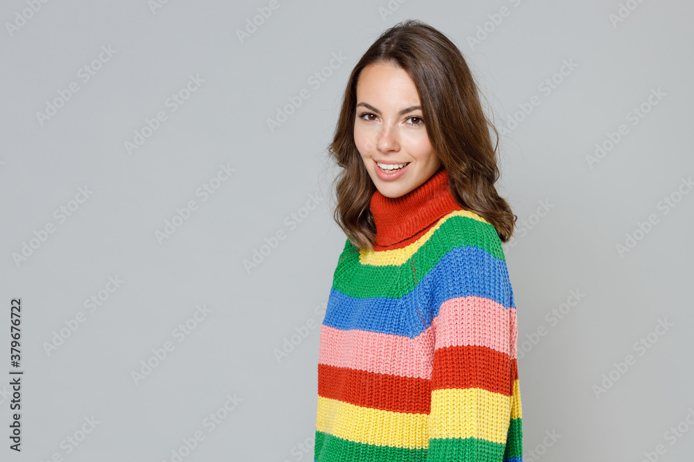 Side view of smiling cheerful charming attractive beautiful young brunette woman 20s wearing casual colorful knitted sweater standing looking camera isolated on grey colour background studio portrait. Side view of smiling cheerful charming attractive beautiful young brunette woman 20s wearing casual colorful knitted sweater standing looking camera isolated on grey colour background studio portrait.